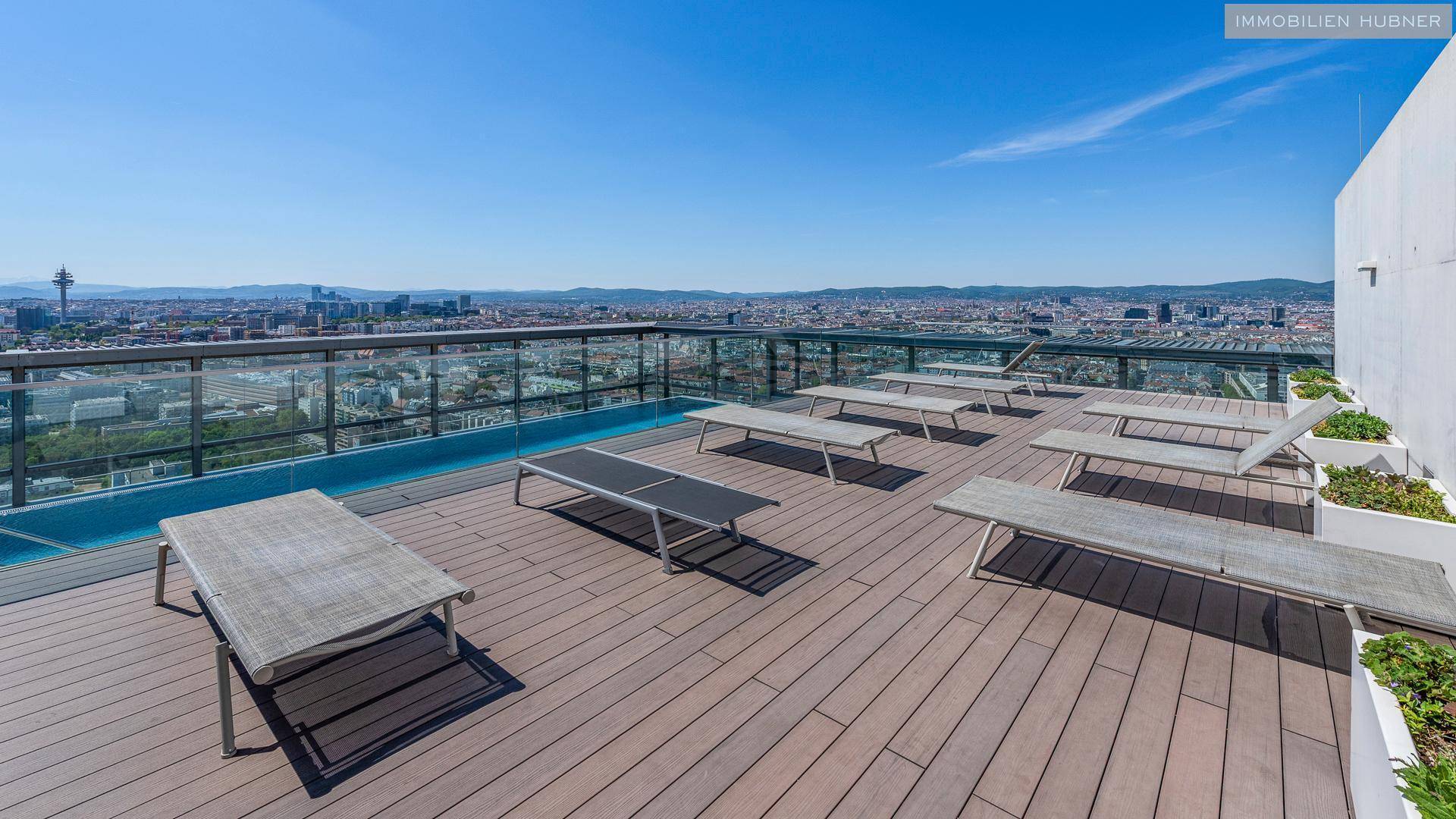 Großzügige Dachterrasse mit Liegestühlen und weitem Blick über die Stadt und den Poolbereich.