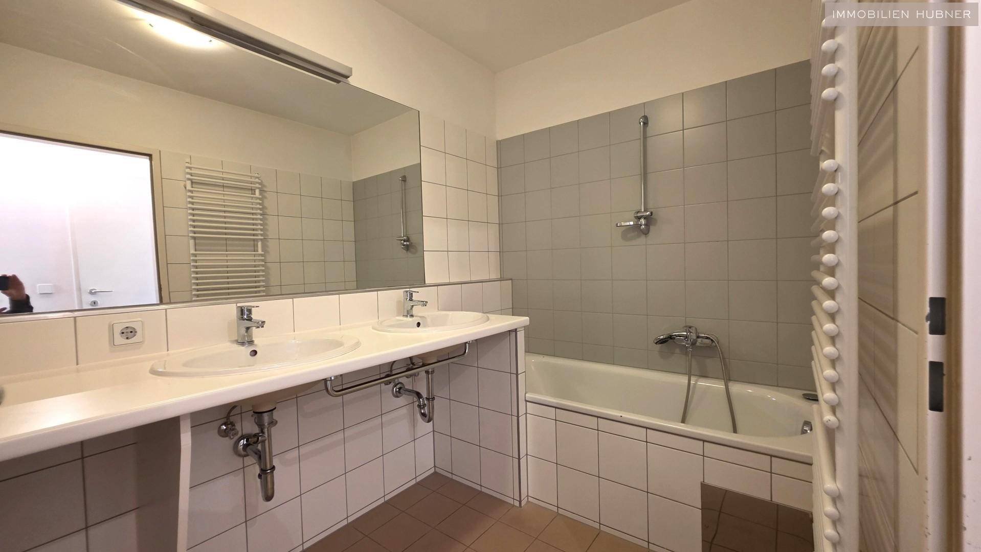 Badezimmer mit Doppelwaschbecken, Badewanne und Fliesen an Wänden und Boden.