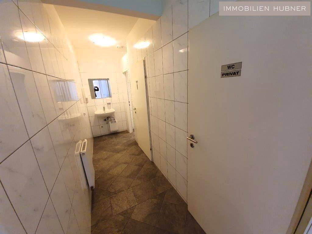 Gefliester Flur mit Zugang zu mehreren Toiletten, ausgestattet mit Waschbecken und Spiegel.