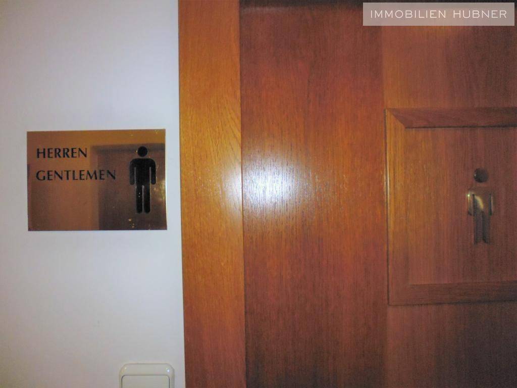 Holztür mit Beschilderung für die Herrentoilette in deutscher und englischer Sprache.
