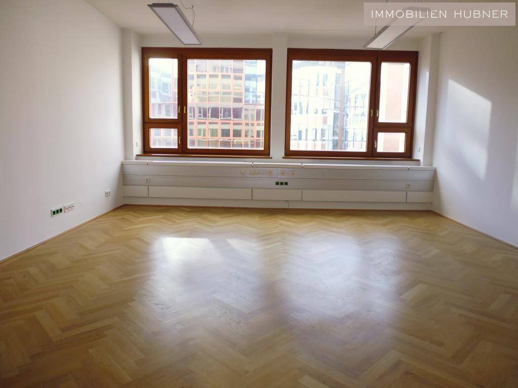 Geräumiges Büro mit viel Tageslicht, Fischgrätparkett und breiter Fensterfront.