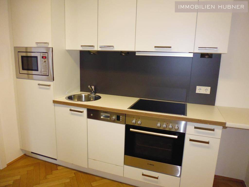 Moderne Einbauküche mit weißen Schränken, Induktionskochfeld, Backofen und Mikrowelle.