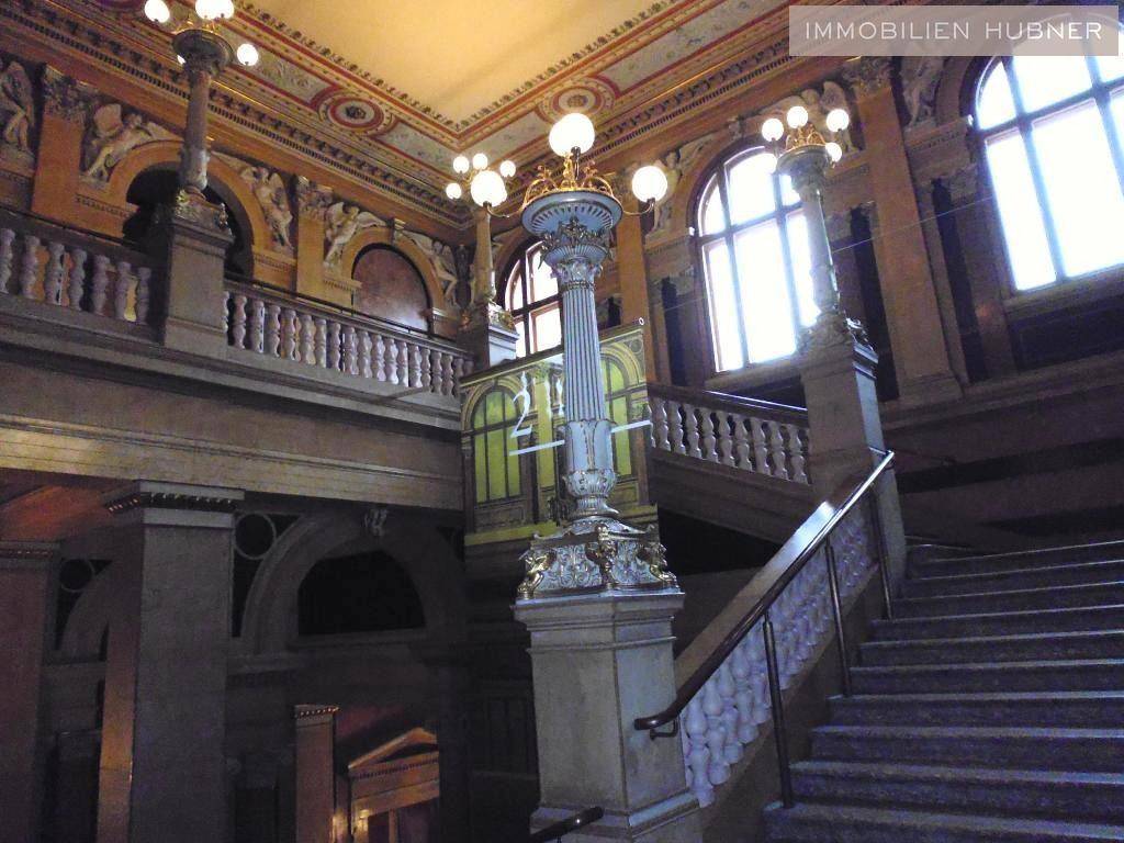 Prunkvolles Treppenhaus in einem Altbau mit hohen Decken, verzierten Säulen und großen Fenstern.
