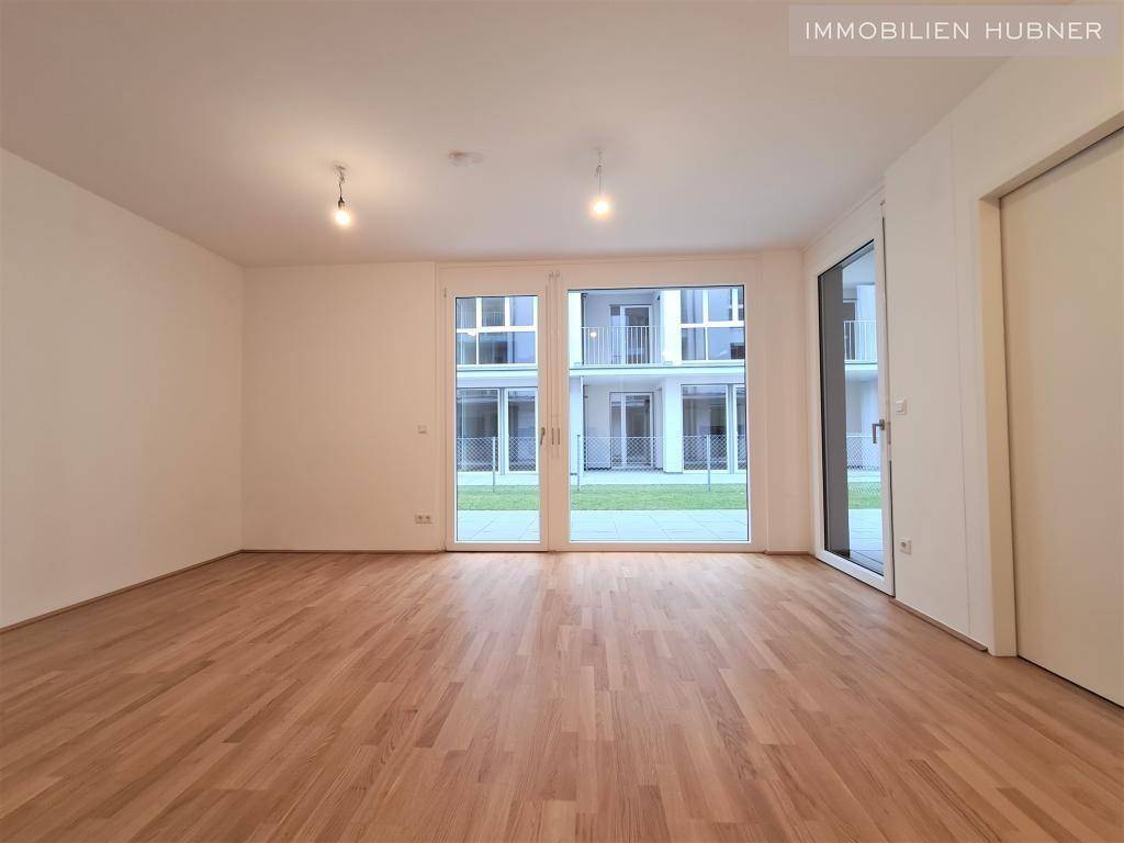 Heller Wohnraum mit Parkettboden und großen Fenstertüren, die viel Tageslicht hereinlassen.