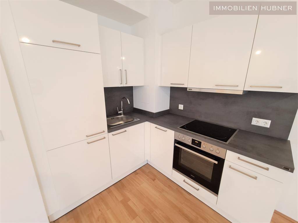 Moderne Einbauküche mit weißen Hochglanzfronten, dunkler Arbeitsplatte und integrierten Geräten.