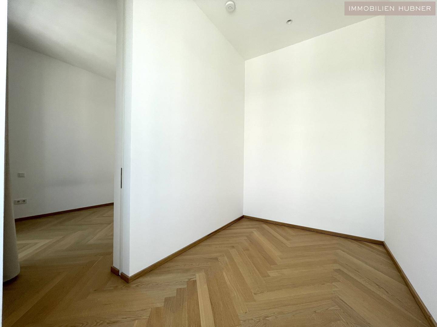 Heller Raum mit Fischgrätparkett und weißen Wänden, vielseitig nutzbar.