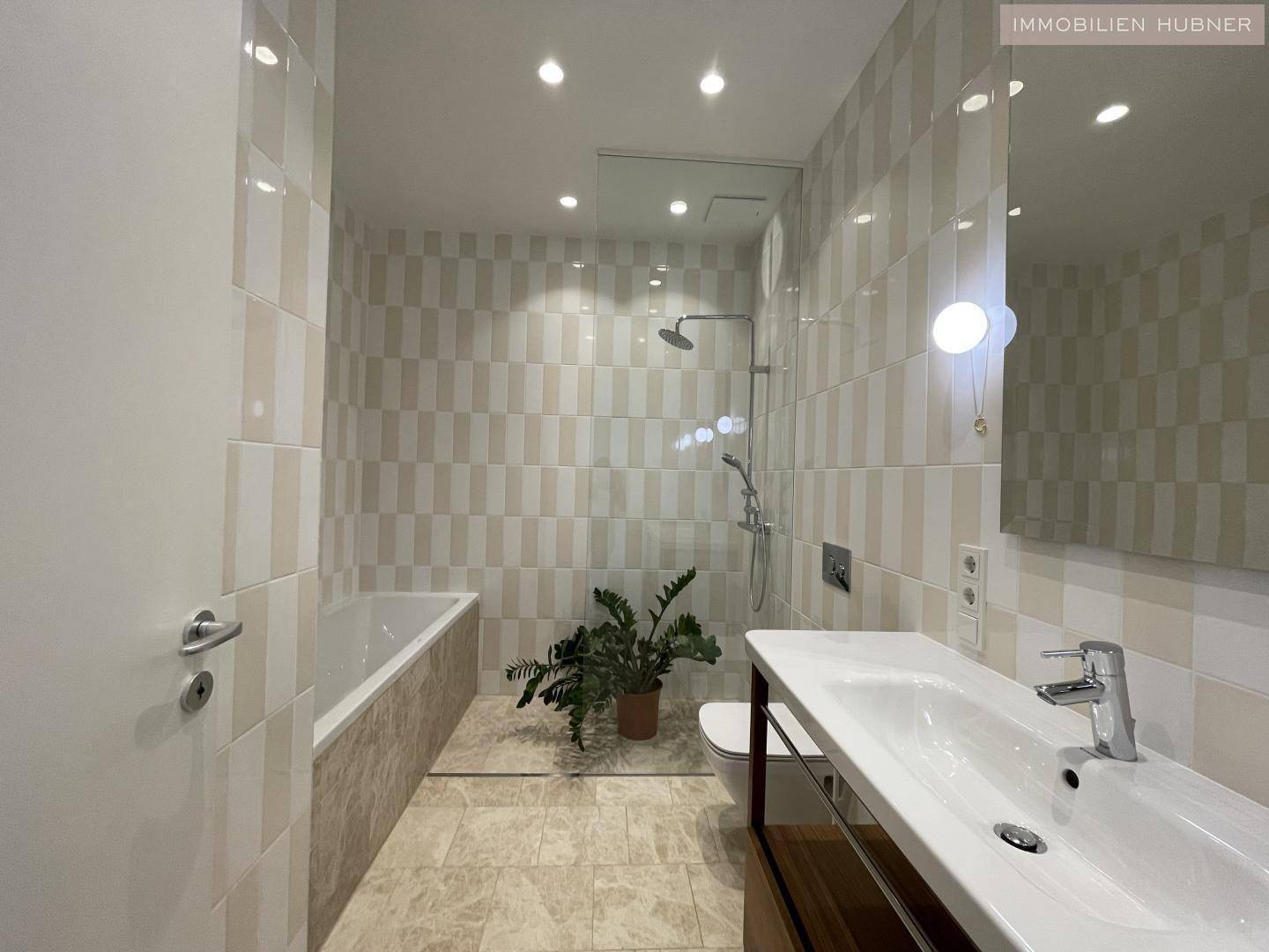Helles Badezimmer mit Badewanne, Dusche, modernem Waschtisch und beigefarbenen Fliesen.