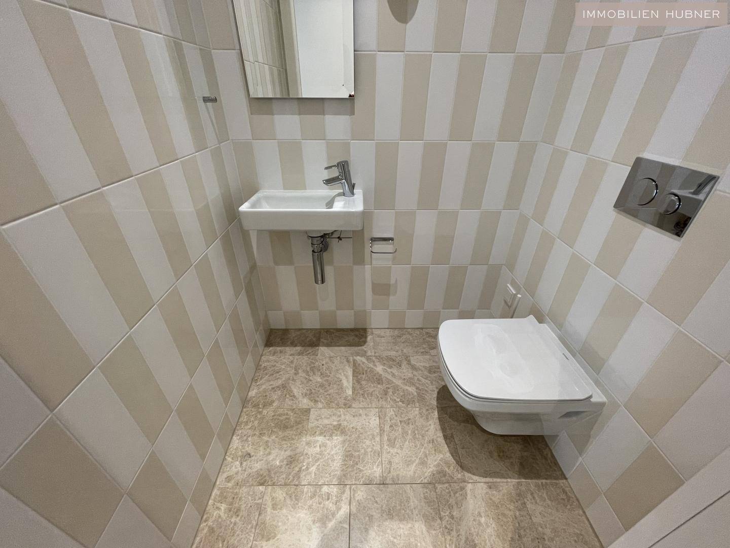 Separates Gäste-WC mit wandhängender Toilette, kleinem Waschbecken und gestreiften Fliesen.