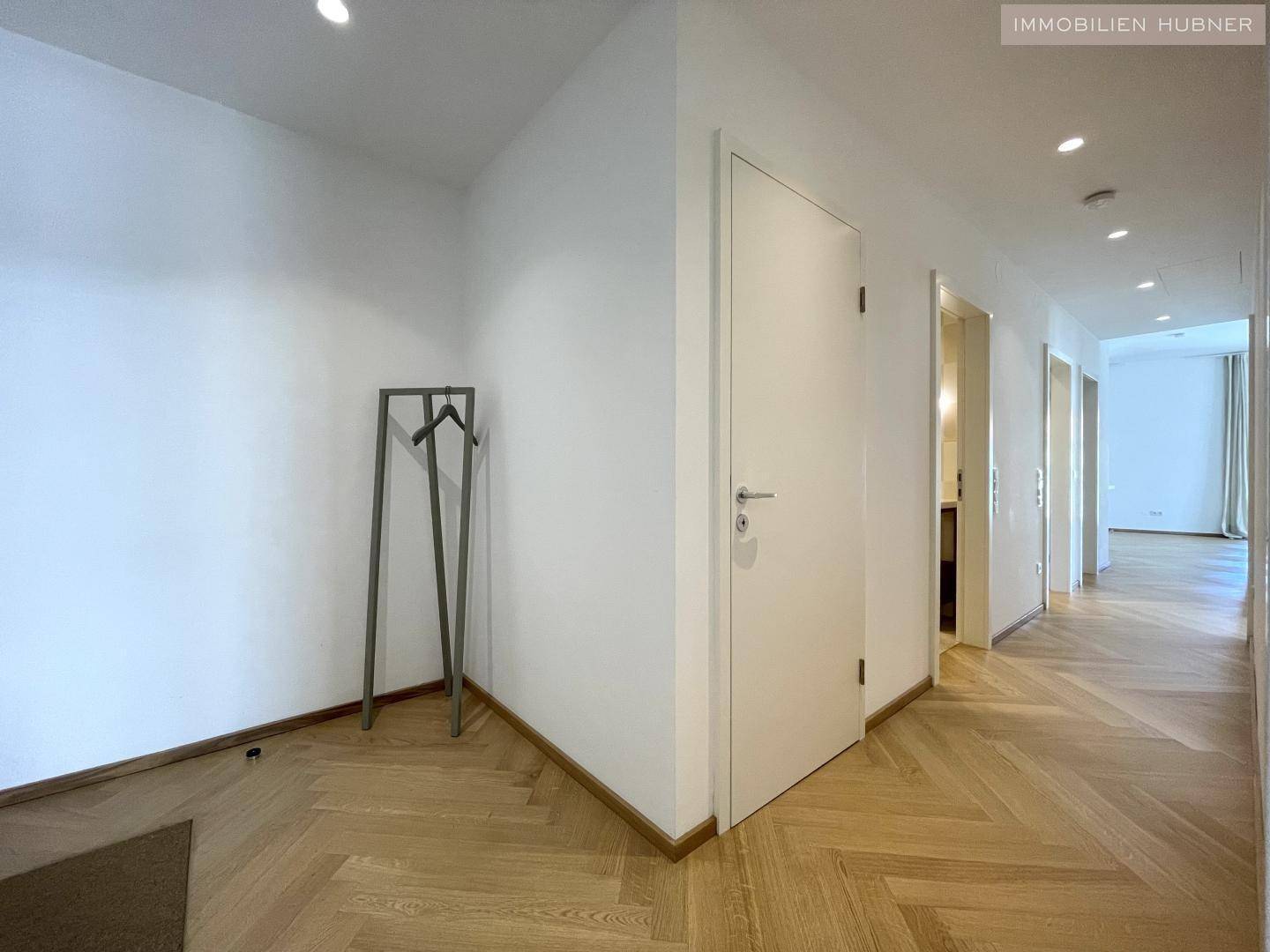 Heller Flur mit elegantem Fischgrätparkett, weißen Wänden und modernen Einbaustrahlern.