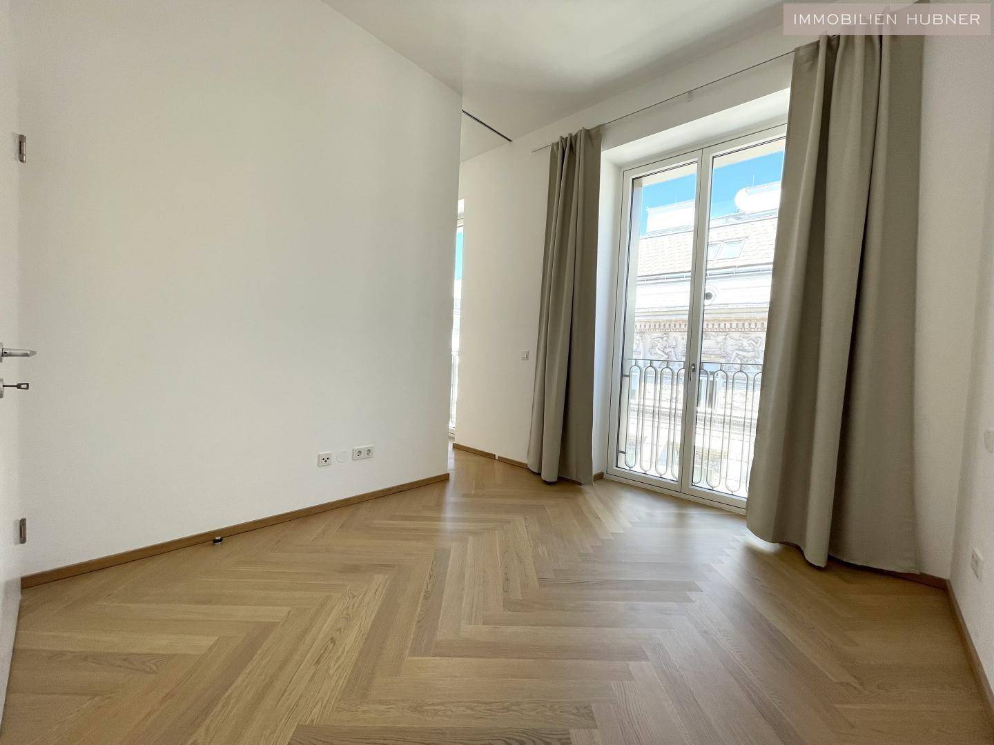 Helles Schlafzimmer mit Fischgrätparkett und einem großen Fenster mit französischem Balkon.