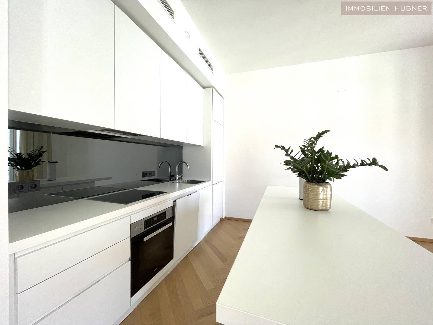 Detailansicht der modernen weißen Küche mit Induktionskochfeld, Backofen und eleganter Spiegelrückwand.