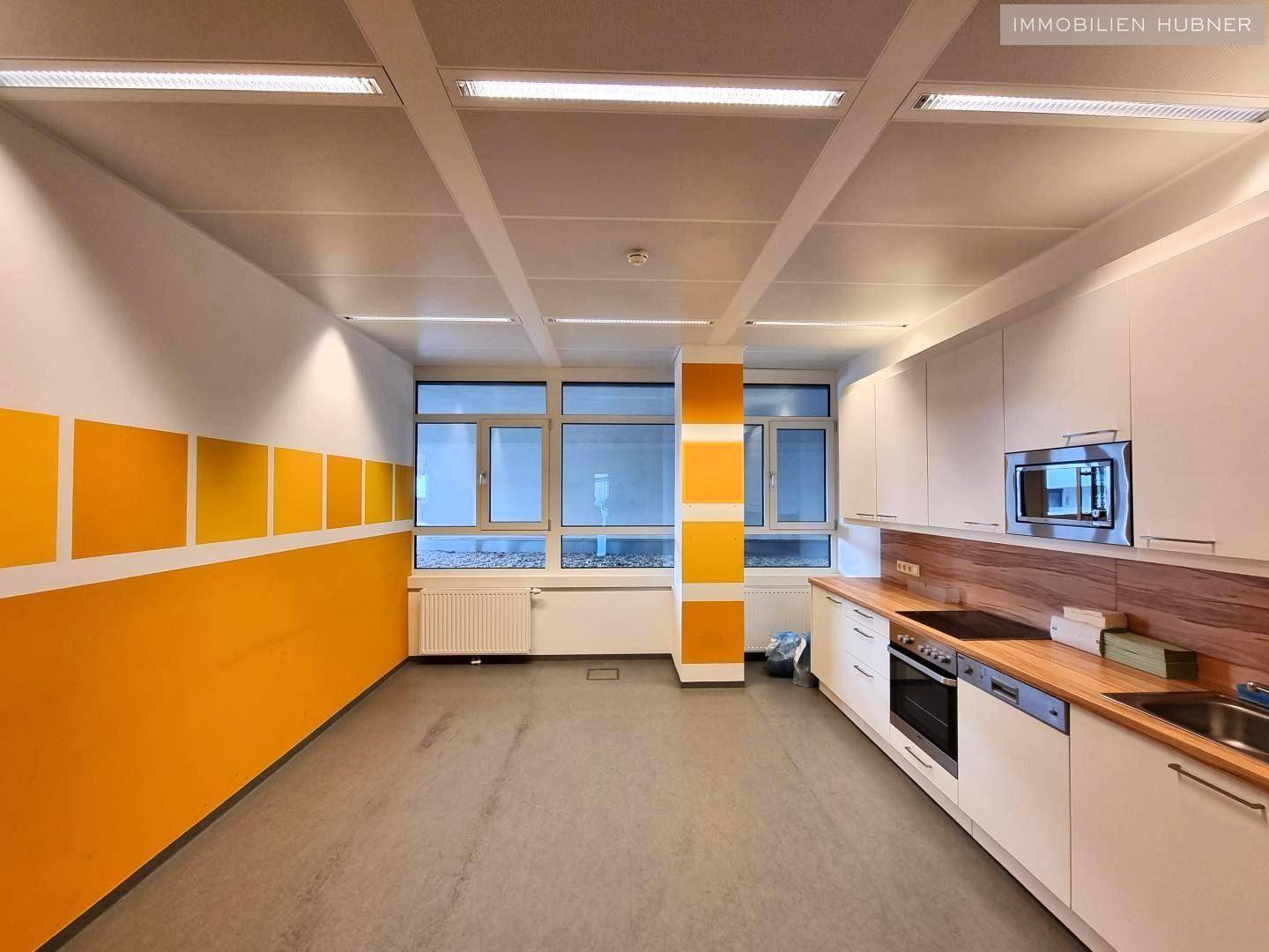 Moderne Teeküche mit orangefarbenen Akzenten, weißen Schränken und integrierten Geräten.