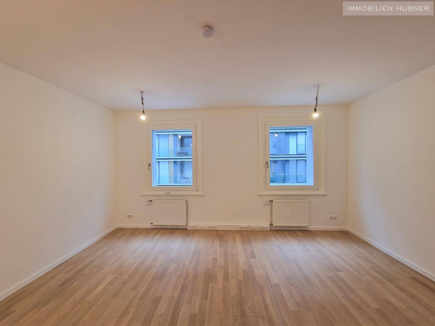 Geräumiger, heller Raum mit Parkettboden und großen Fenstern, ideal für Wohn- oder Arbeitszwecke.