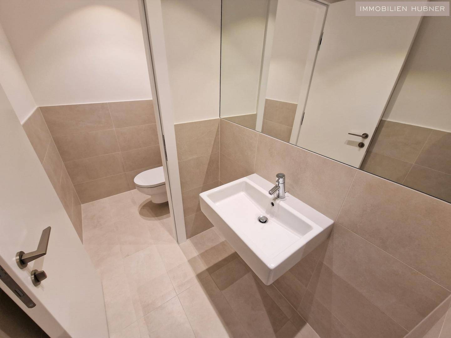 Helles Gäste-WC mit modernem Design, Wand-WC und großem Spiegel, in einwandfreiem Zustand.