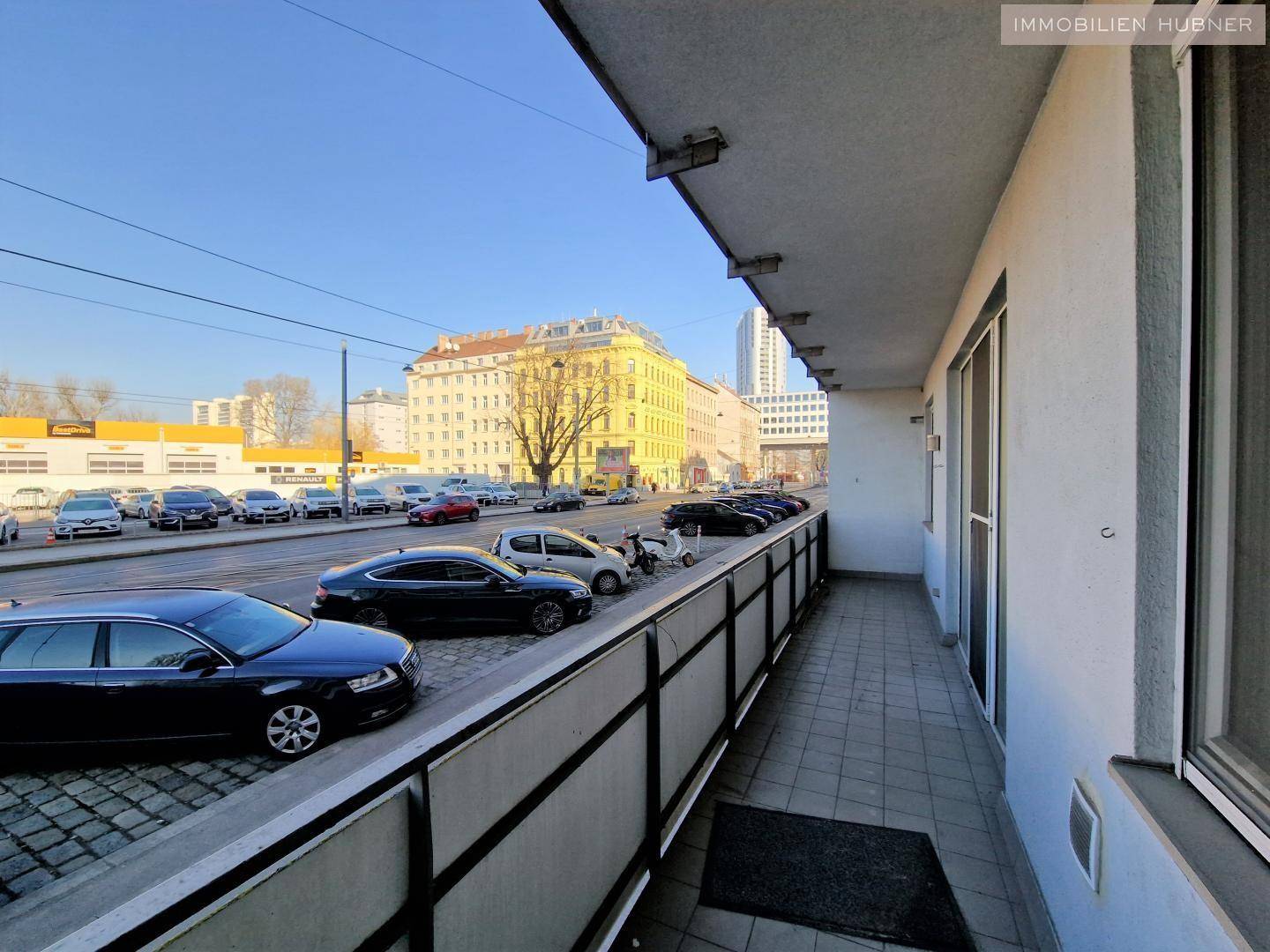 Langer Balkon mit Blick auf eine belebte Straße und städtische Umgebung.
