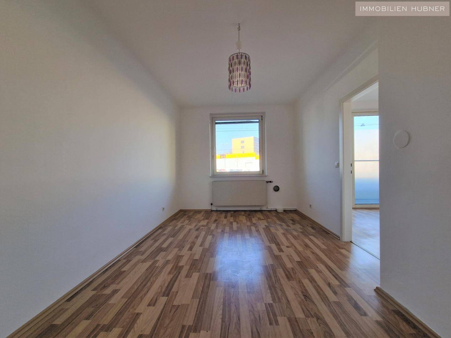 Helles Zimmer mit Laminatboden und Fenster, geeignet als Wohn- oder Schlafzimmer.