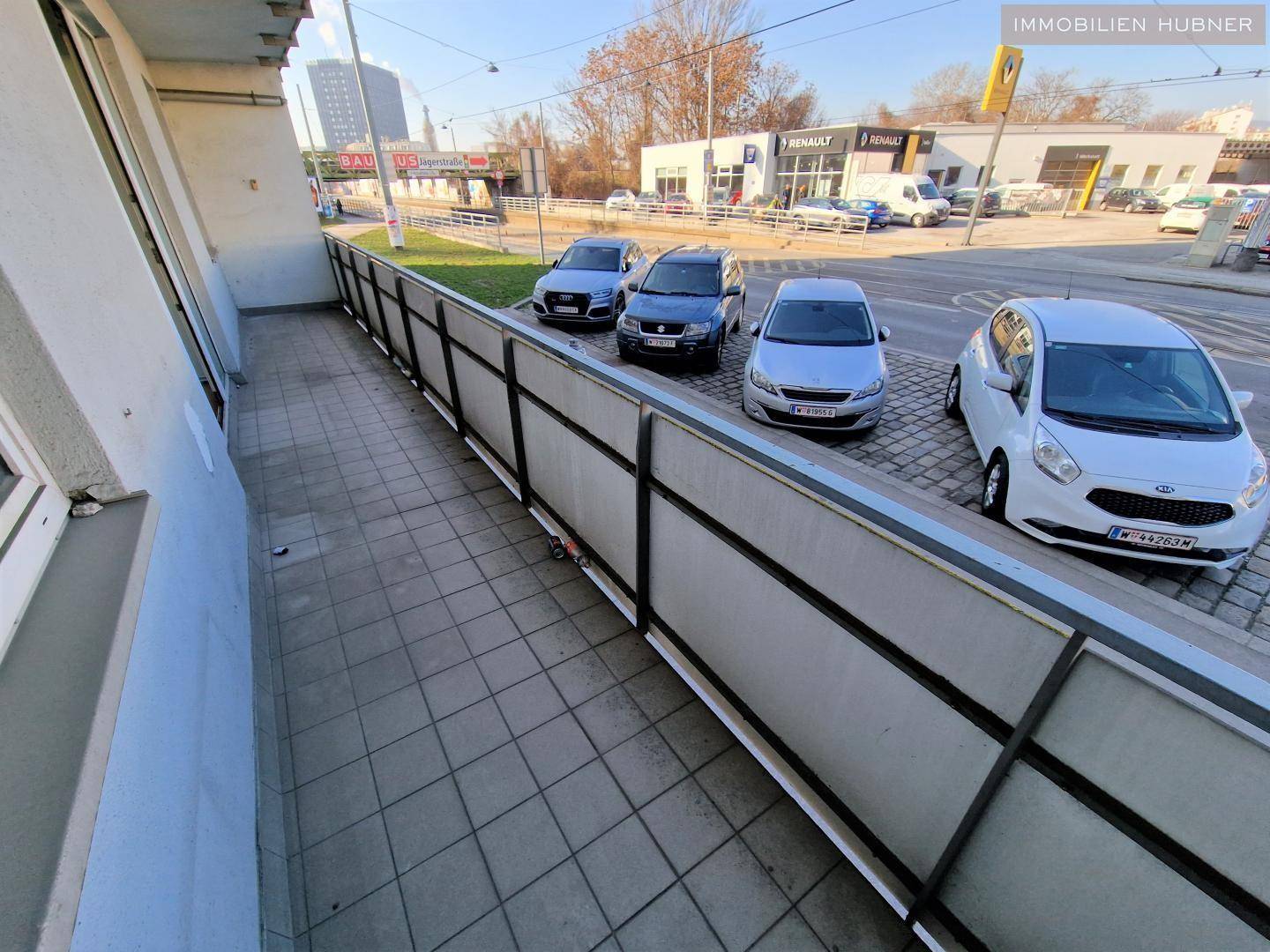 Langer Balkon mit Fliesenboden und Blick auf die Straße und umliegende Gebäude.