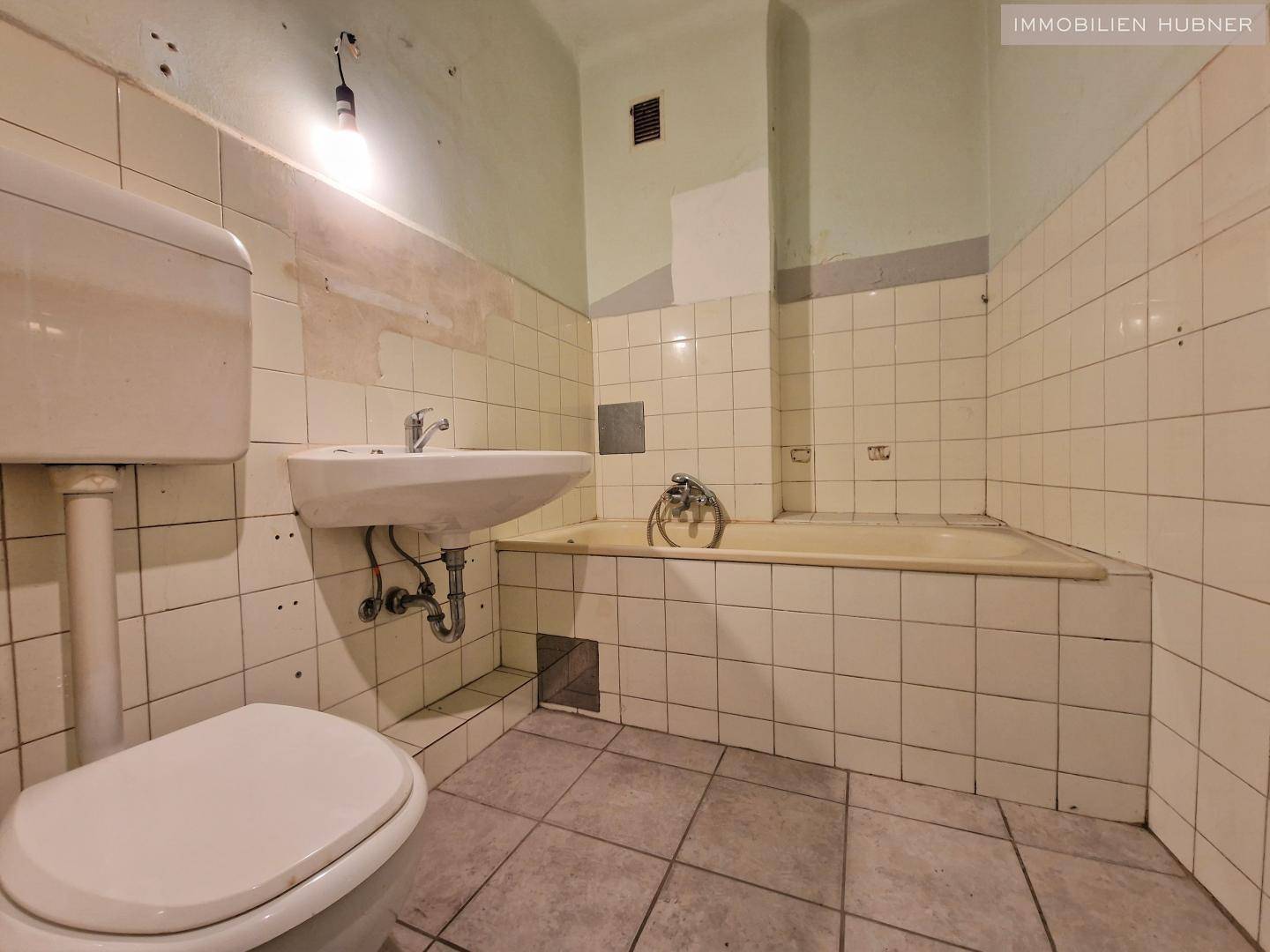 Veraltetes Badezimmer in sanierungsbedürftigem Zustand mit Badewanne, Waschbecken und Toilette.