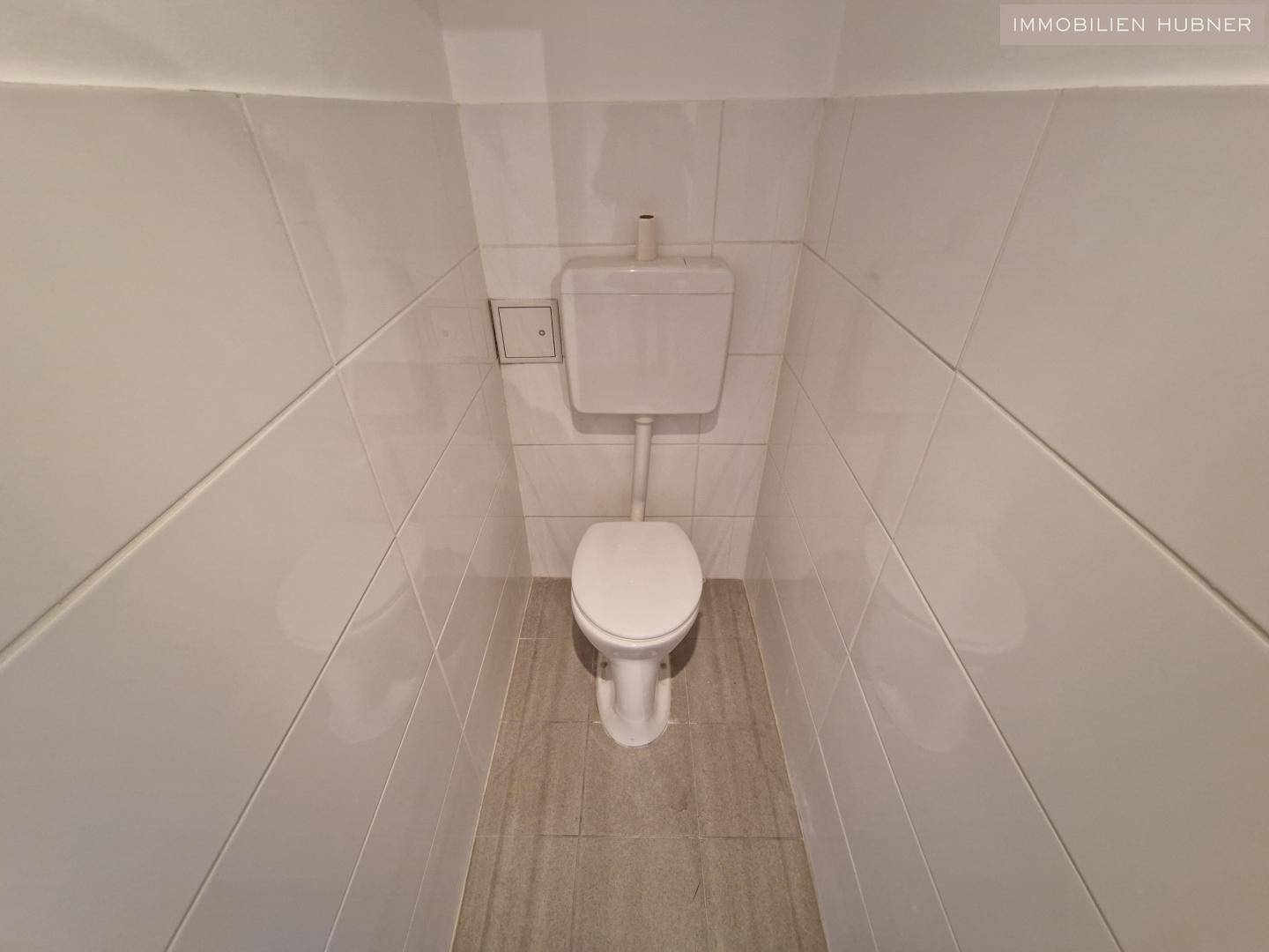 Separates WC mit weißen Fliesen und einer Standardtoilette.
