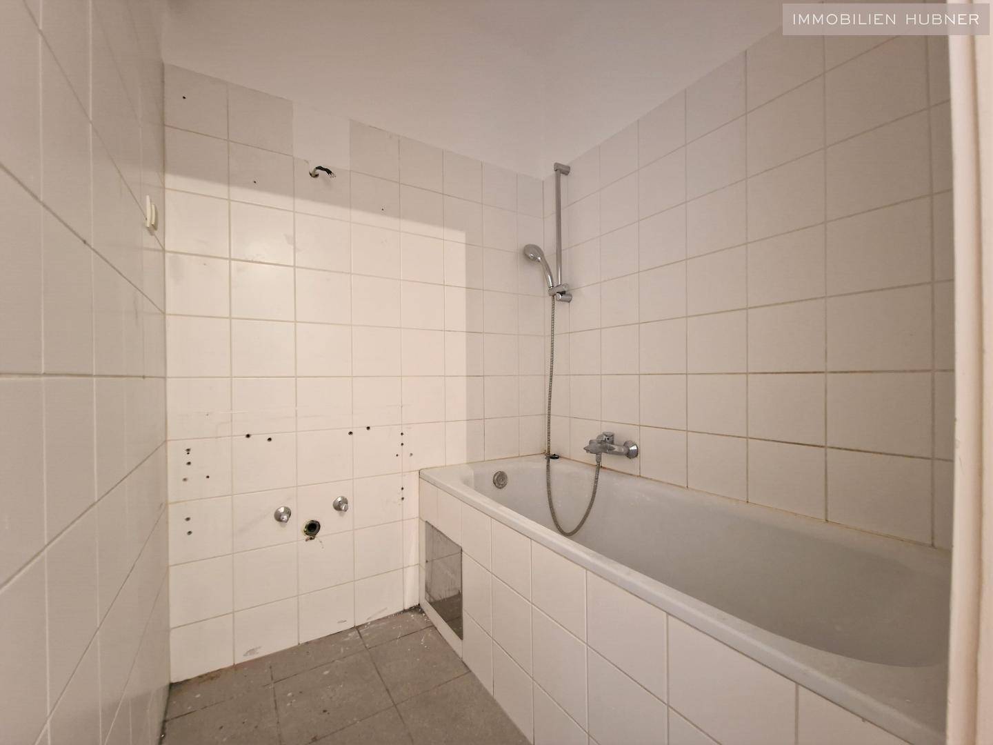 Badezimmer mit weiß gefliesten Wänden und einer Badewanne mit Duschfunktion.