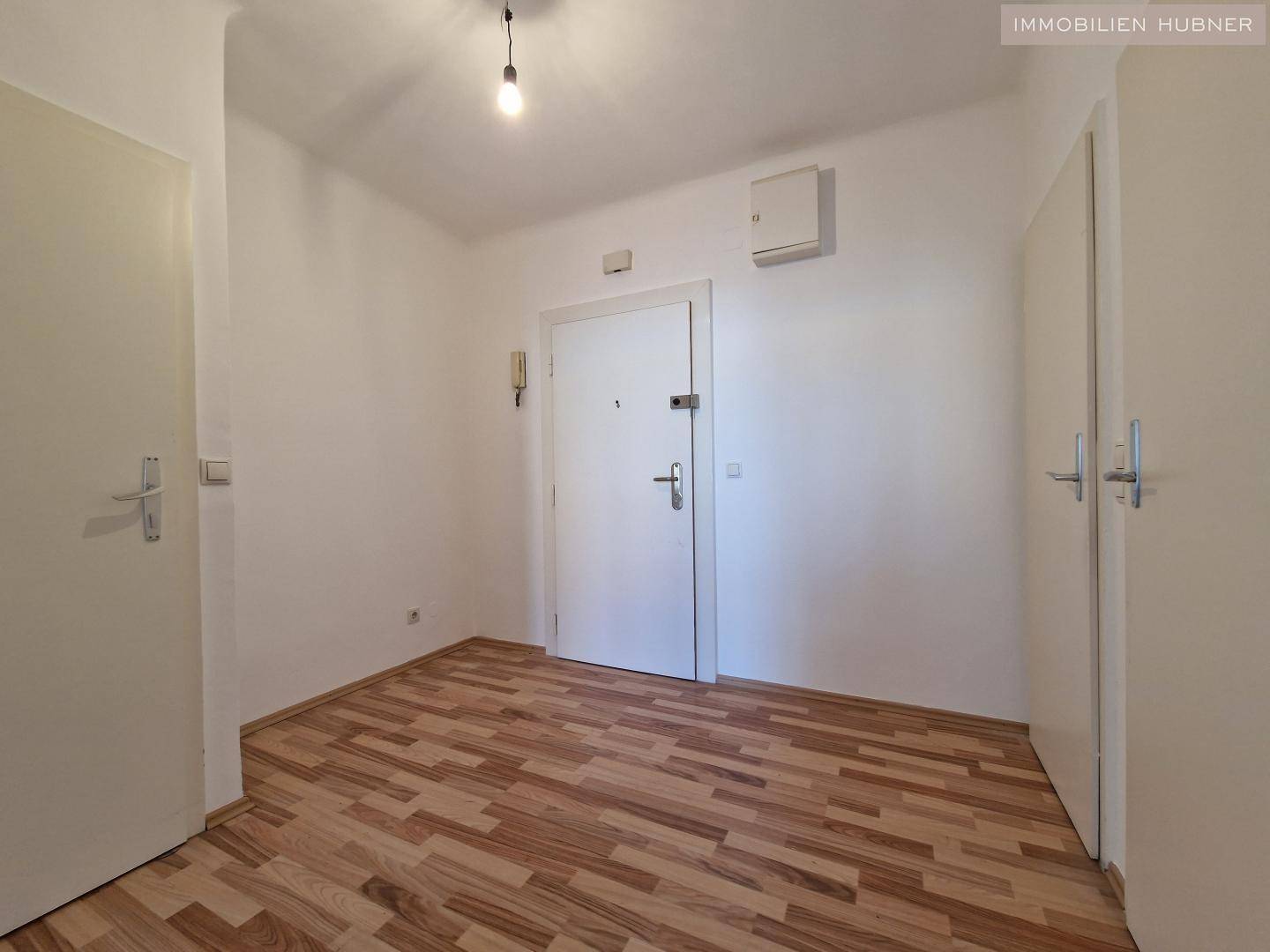 Eingangsbereich mit Laminatboden und weiß gestrichenen Wänden, inklusive Haustür.