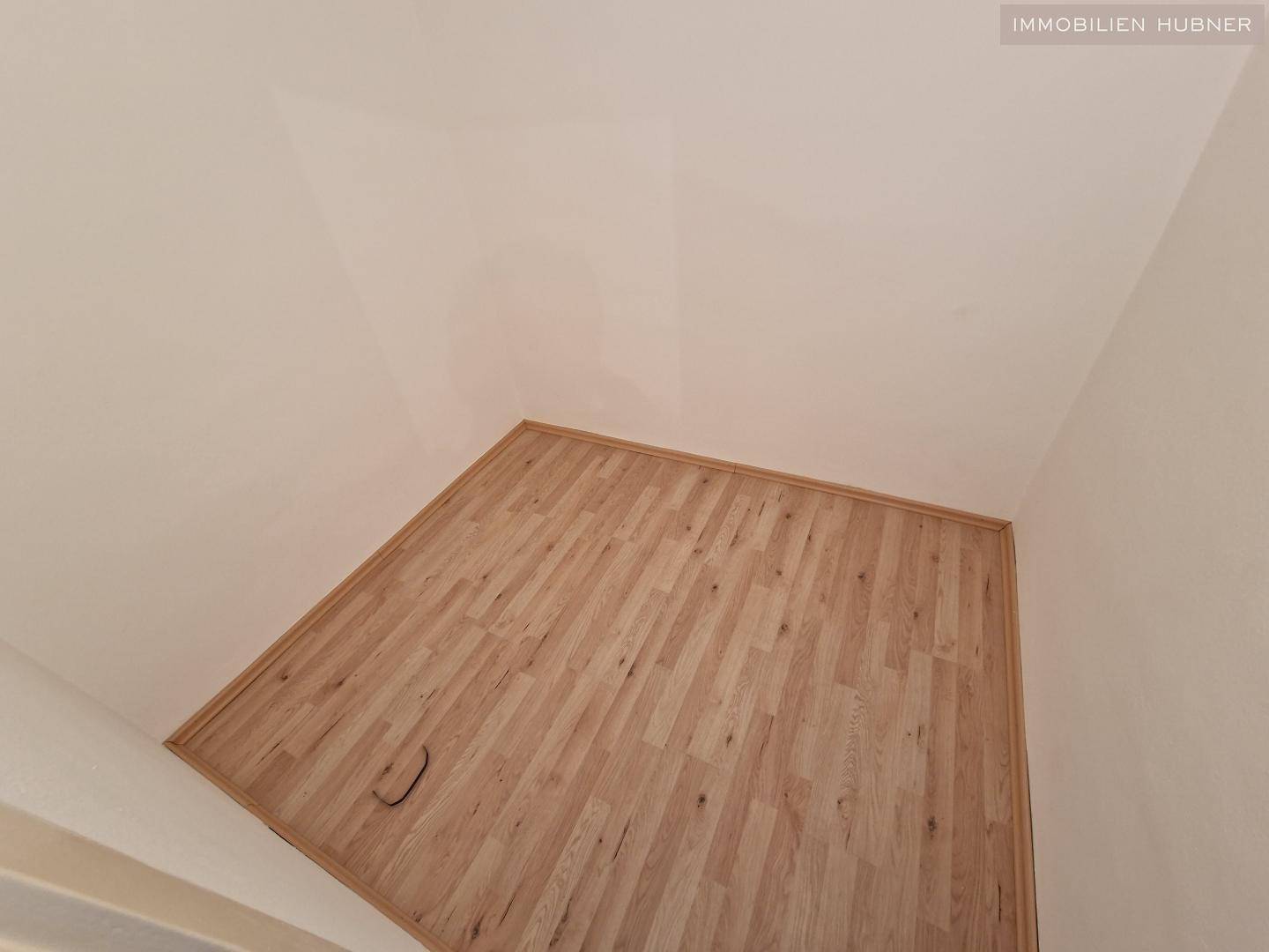Ecke eines Raumes mit Laminatboden und weißen Wänden, die eine saubere Oberfläche zeigen.