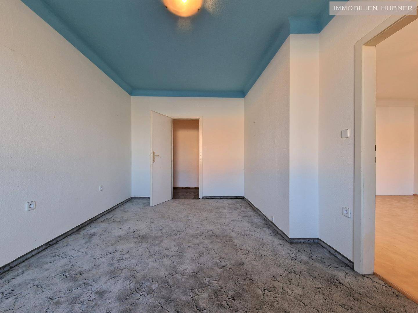 Geräumiges Zimmer mit Teppichboden, blauer Decke und Zugang zu einem weiteren Raum.