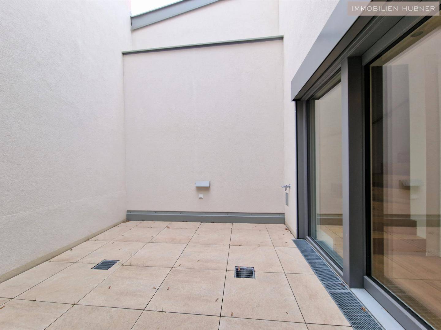 Kleine, geflieste Terrasse mit Entwässerungssystem und Zugang zum Innenbereich des Hauses.