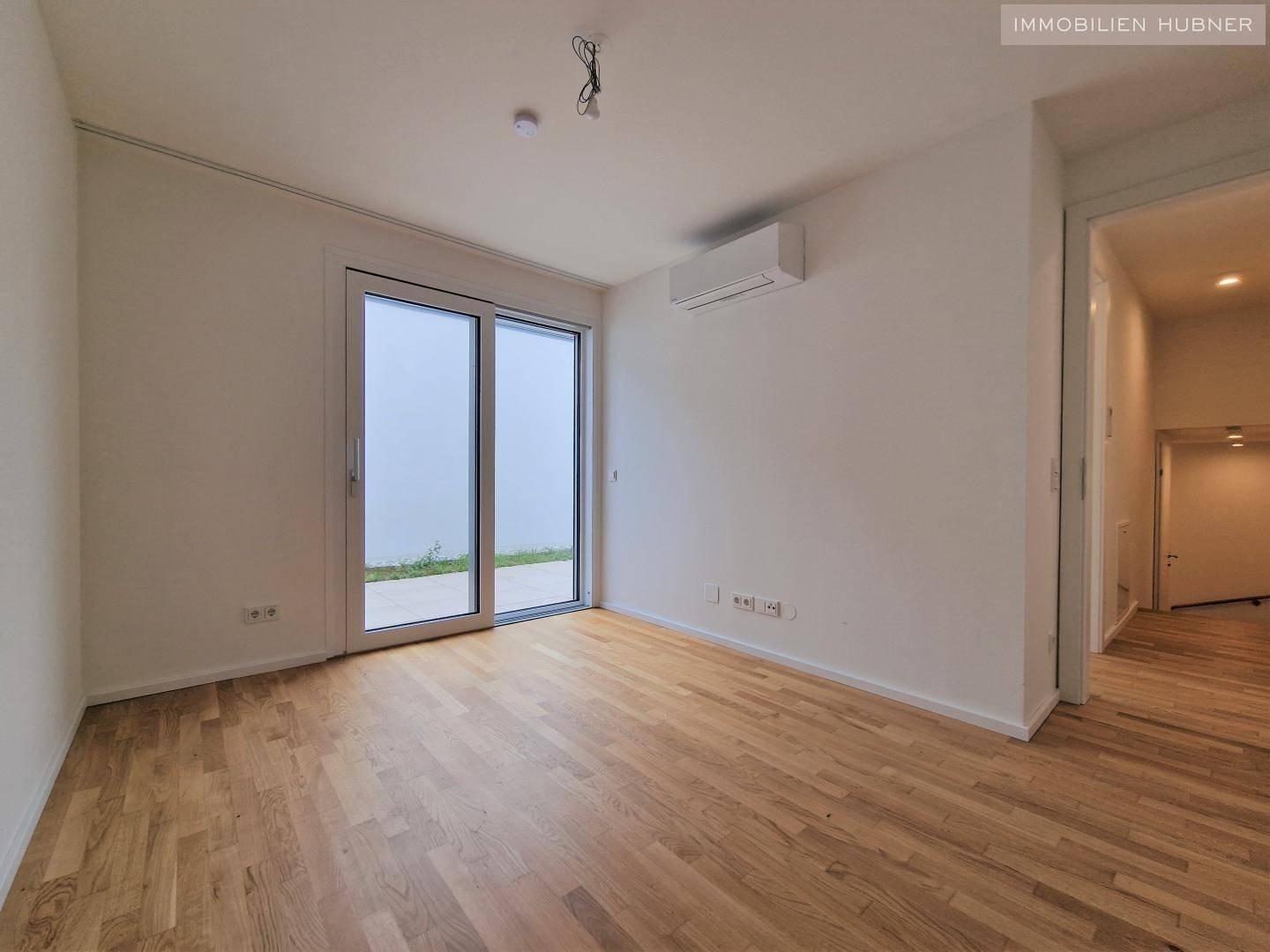 Helles Schlafzimmer mit Parkettboden, Klimaanlage und Schiebetür zum Außenbereich.