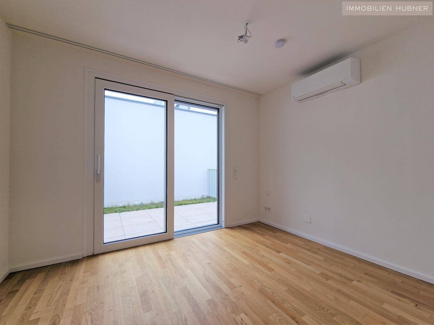 Geräumiges Schlafzimmer mit Holzboden, Klimaanlage und Zugang zu einem kleinen Außenbereich.