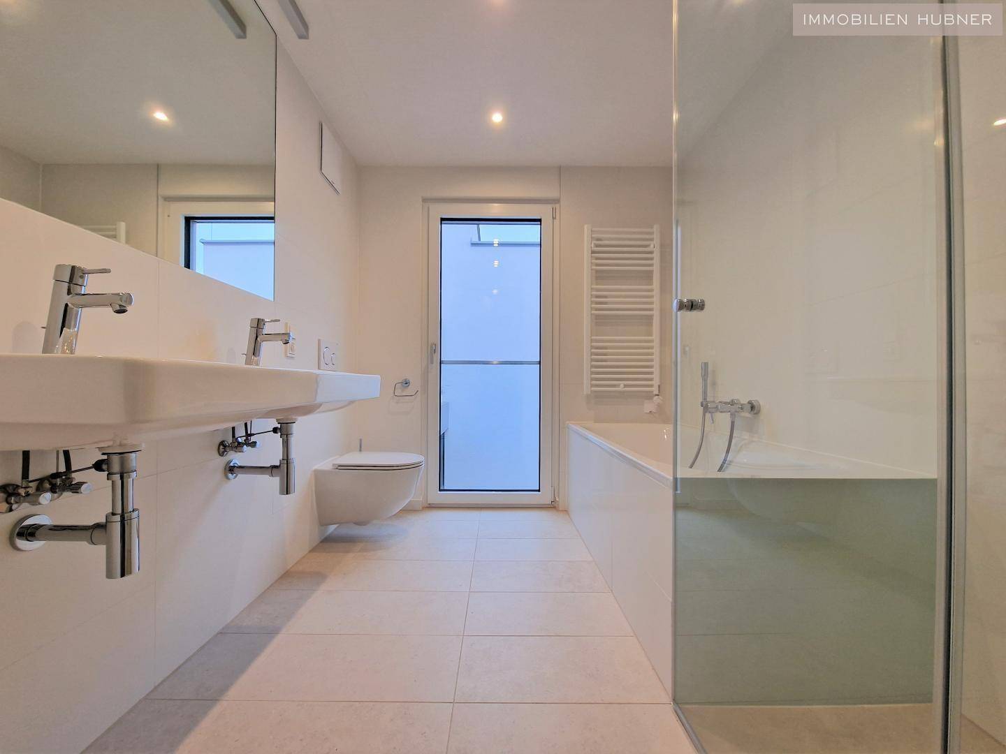Modernes Badezimmer mit Doppelwaschbecken, Badewanne, Dusche und beheiztem Handtuchhalter.