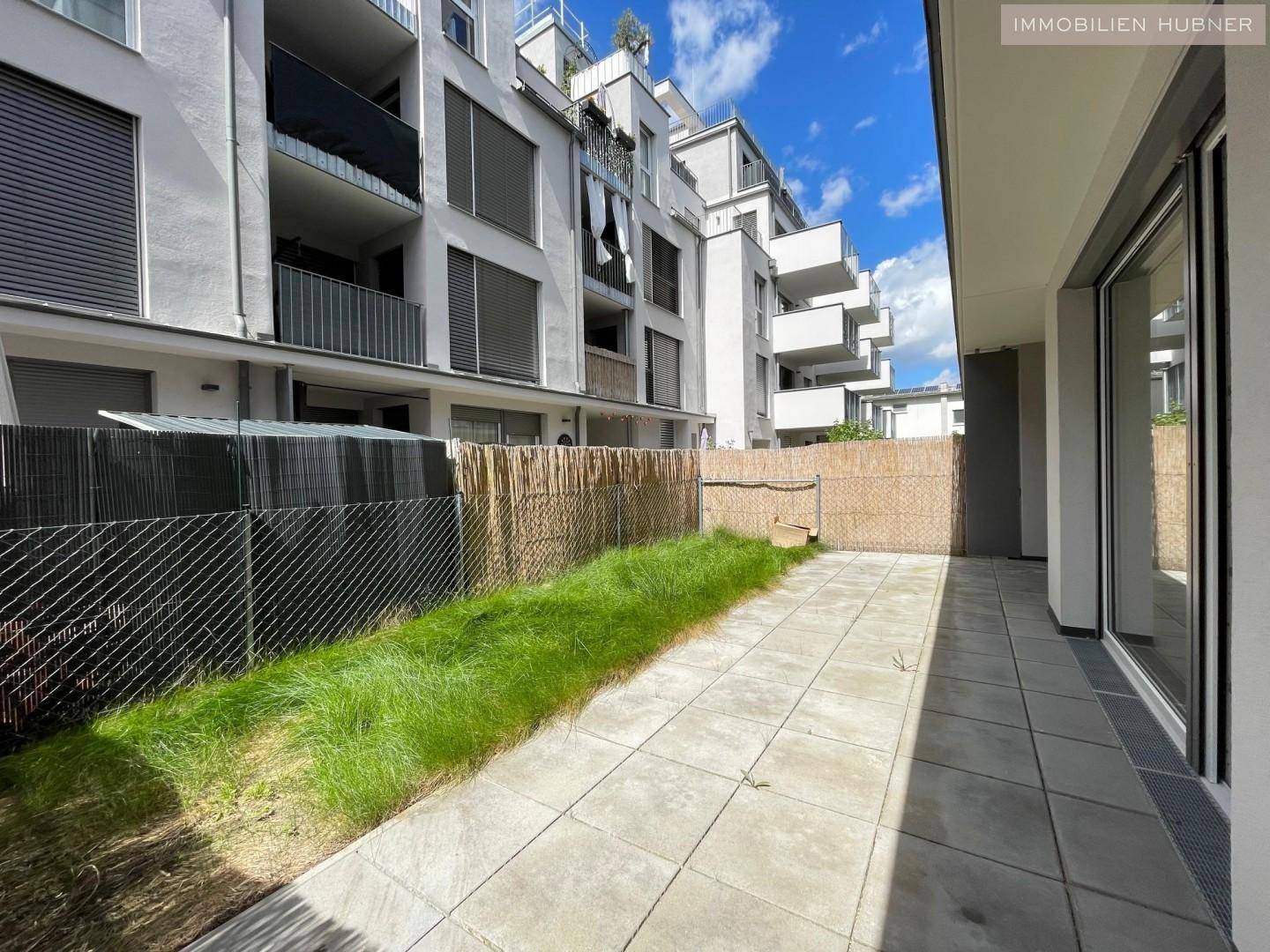 Lange Terrasse mit kleiner Rasenfläche, umgeben von einem Sichtschutz und dem modernen Wohngebäude.