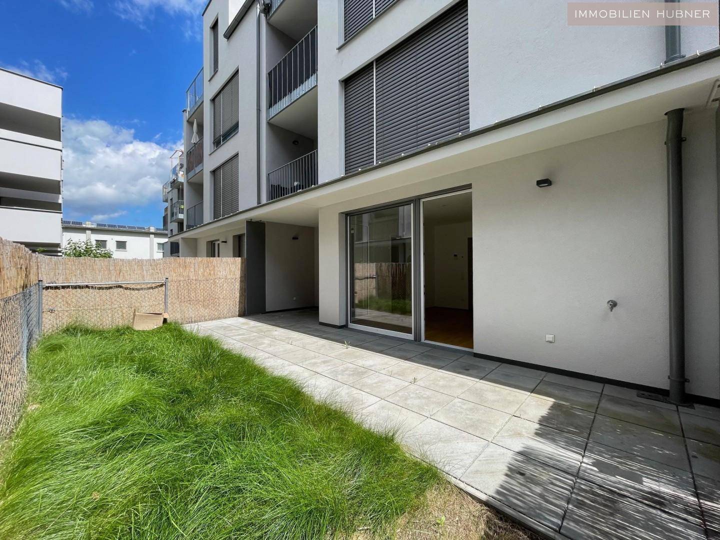 Sonniger Außenbereich mit gepflasterter Terrasse und kleiner Grünfläche vor dem modernen Gebäude.