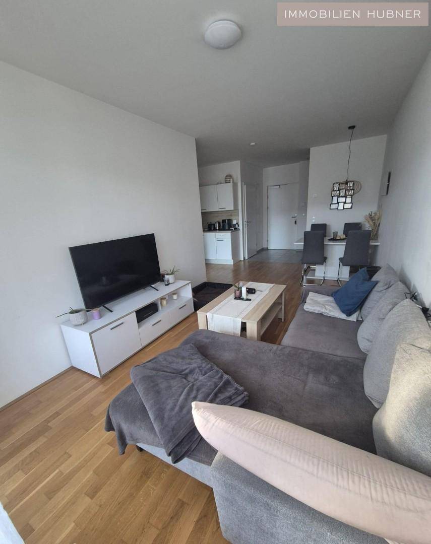 Heller Wohn-Essbereich mit Sofa, Fernseher und Esstisch, offener Zugang zur Küche.