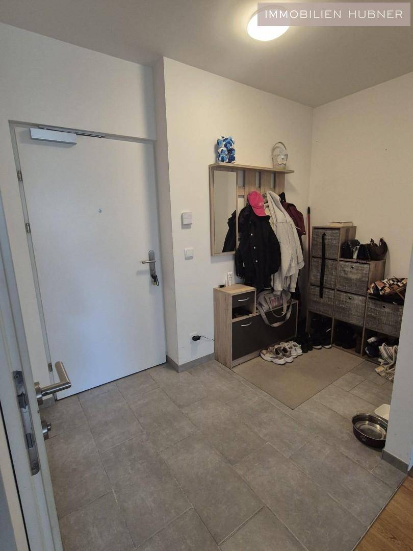 Eingangsbereich mit Fliesenboden, Garderobe und Schuhschränken, hell beleuchtet.