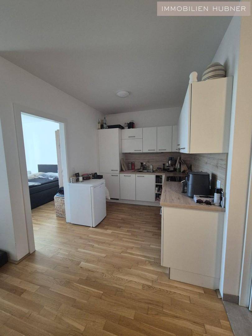 Funktionale Küche mit weißen Schränken und Holzarbeitsplatte, offen zum Schlafzimmer.