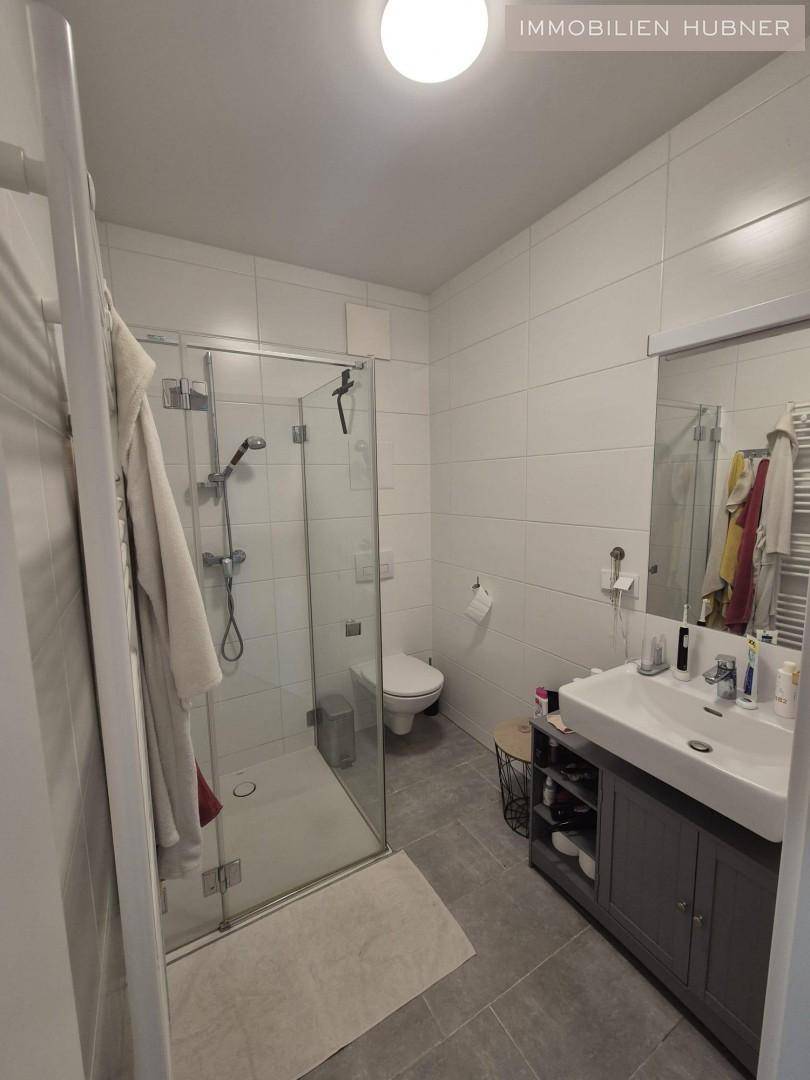 Modernes Badezimmer mit weißen Fliesen, ebenerdiger Dusche und Einzelwaschbecken.