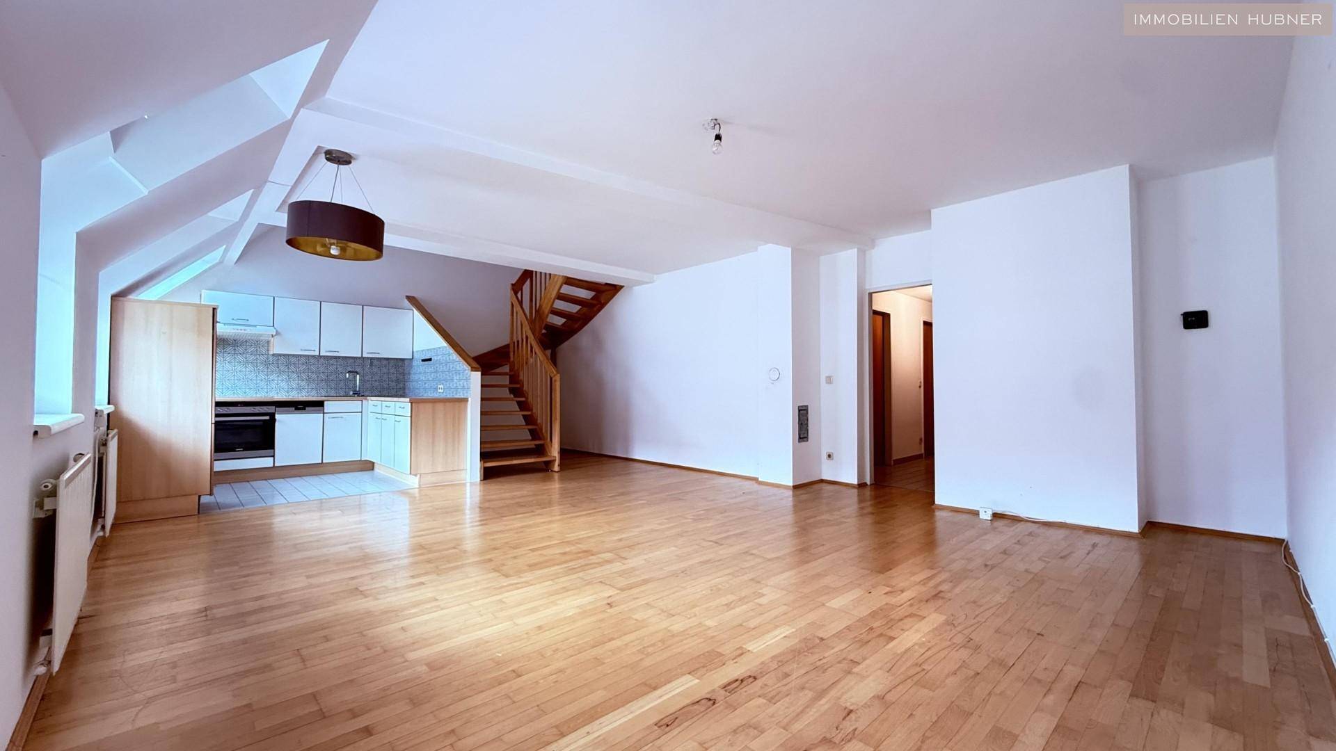 Geräumiger Wohnbereich mit Parkettboden, offener Küche und Holztreppe, die in die obere Etage führt.