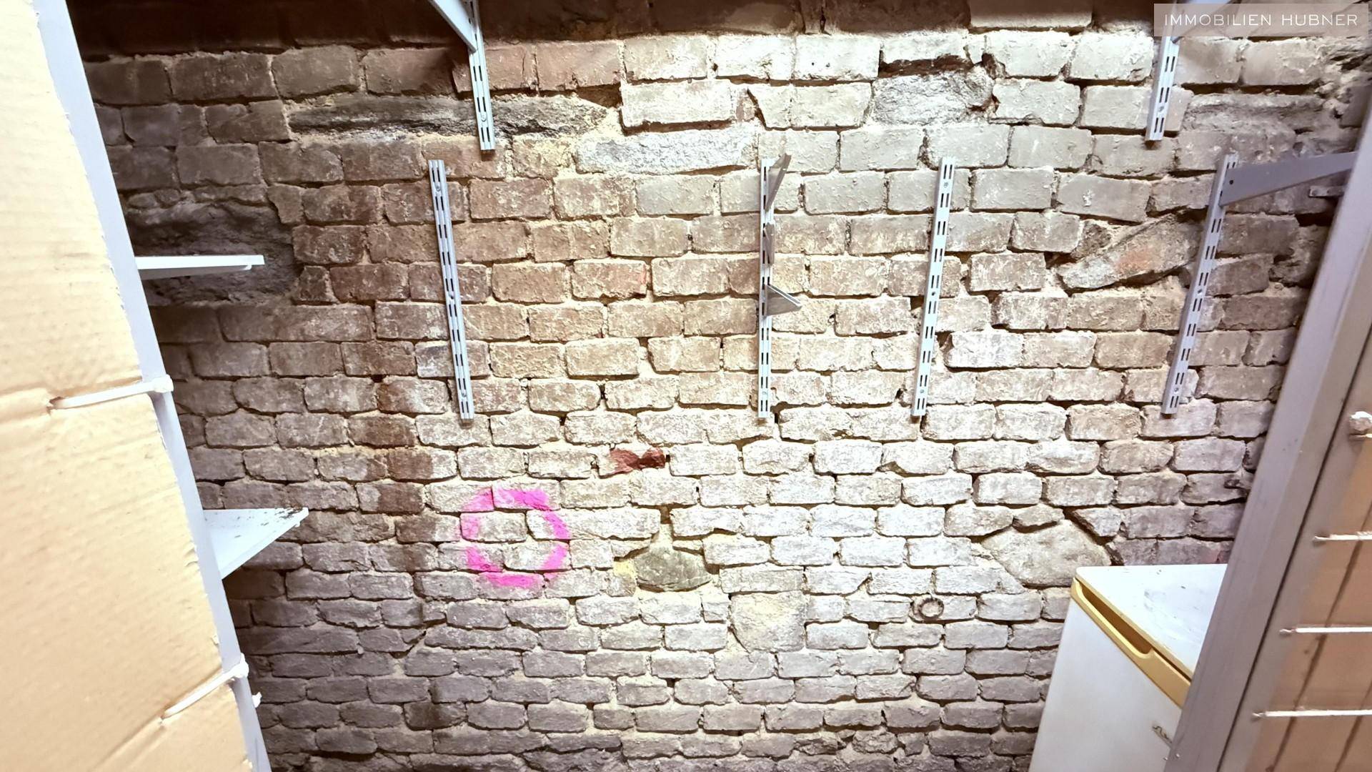 Detailansicht einer unverputzten Ziegelwand im Keller mit montierten Regalhalterungen.
