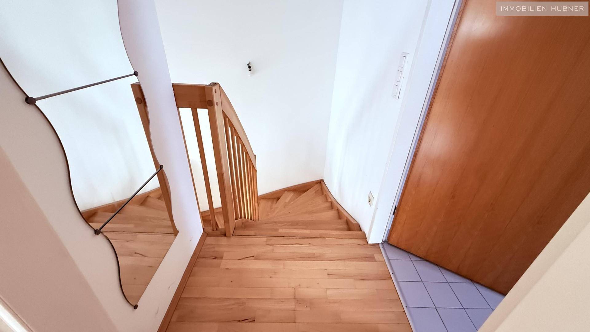 Aufwärtsblick auf die helle Holztreppe mit einem Spiegel an der Wand, der den Raum optisch erweitert.