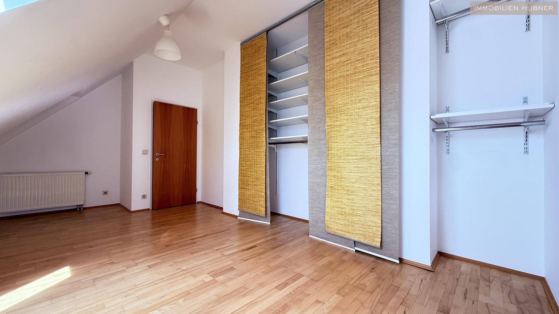 Geräumiges Zimmer mit Holzboden und einem offenen Schranksystem mit Regalen und Kleiderstangen.