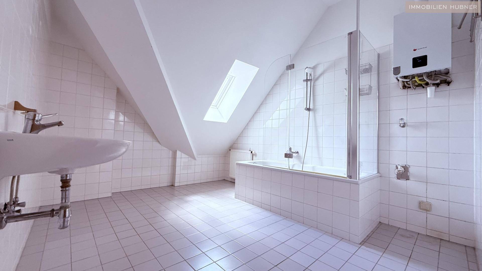 Badezimmer mit weißen Fliesen, Badewanne mit Duschabtrennung und Dachschräge mit Dachfenster.
