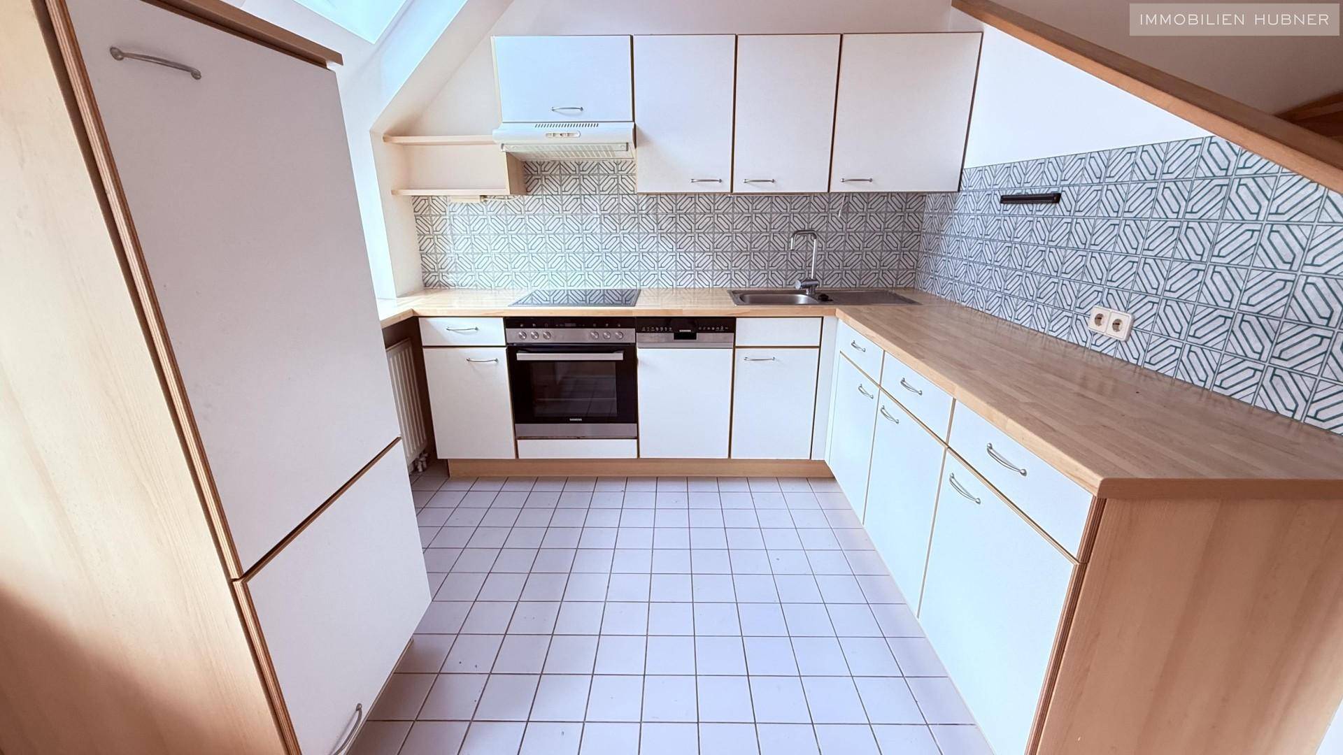 Funktionale Küche mit weißen Schränken, Holz-Arbeitsplatten und gemusterten Fliesen an der Wand.