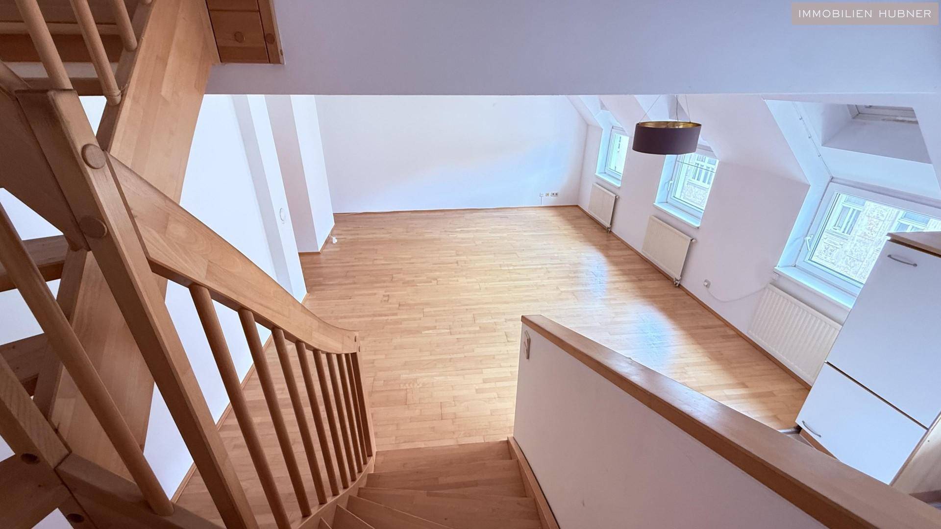 Blick von der Holztreppe hinunter in den hellen Wohnbereich mit Parkettboden und Dachfenstern.