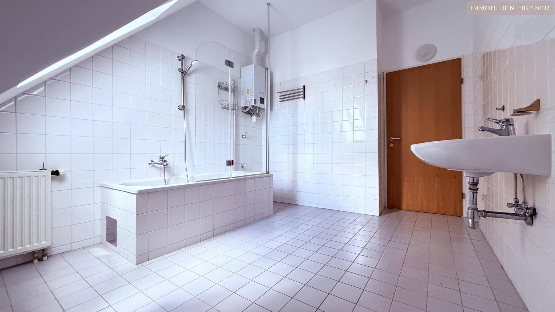 Helles Badezimmer mit Badewanne, Duschvorrichtung und Waschbecken, komplett gefliest in Weiß.
