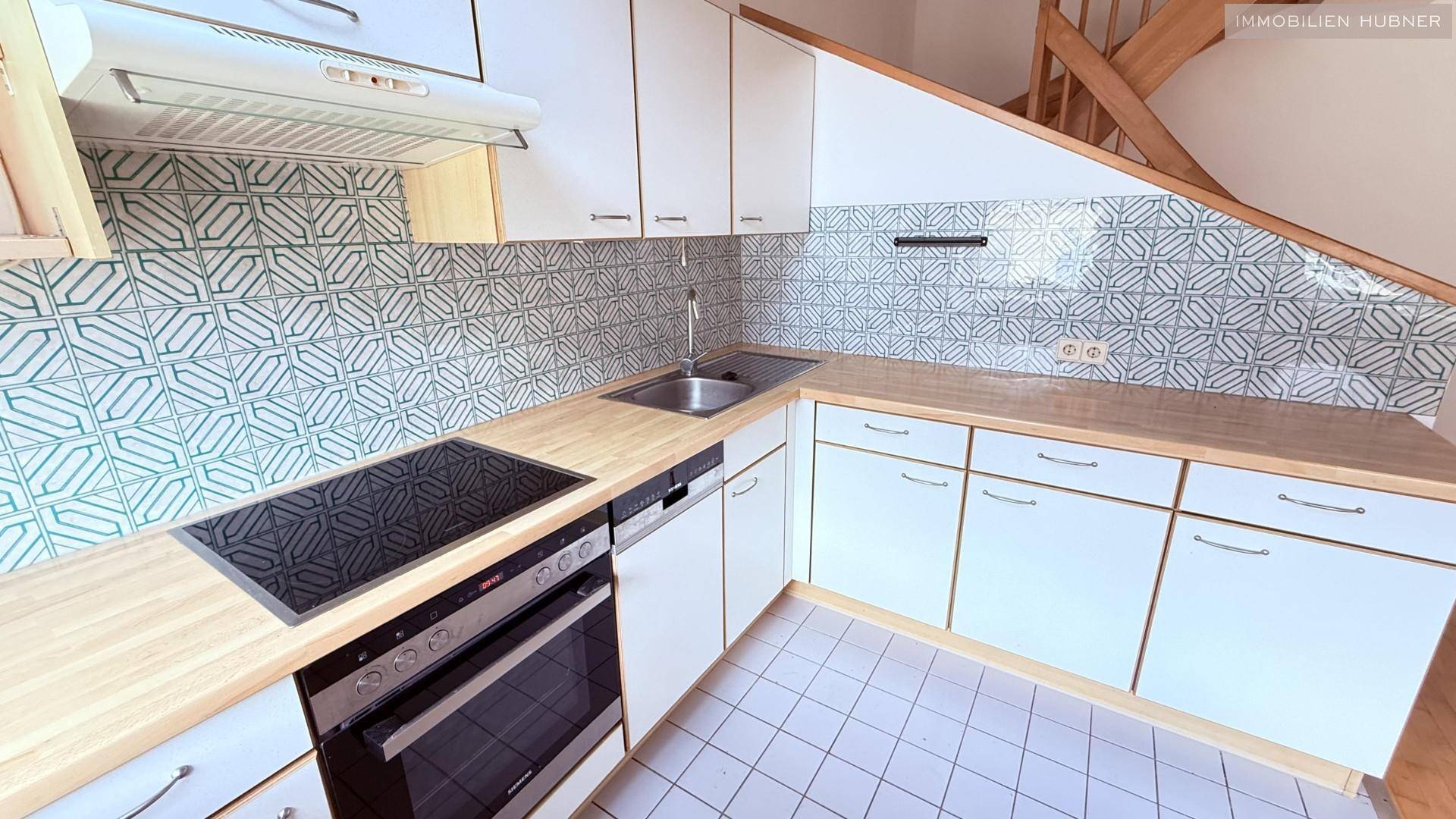 Detailansicht der Küche mit Induktionskochfeld, Backofen und Spüle, umgeben von weißen Schränken.