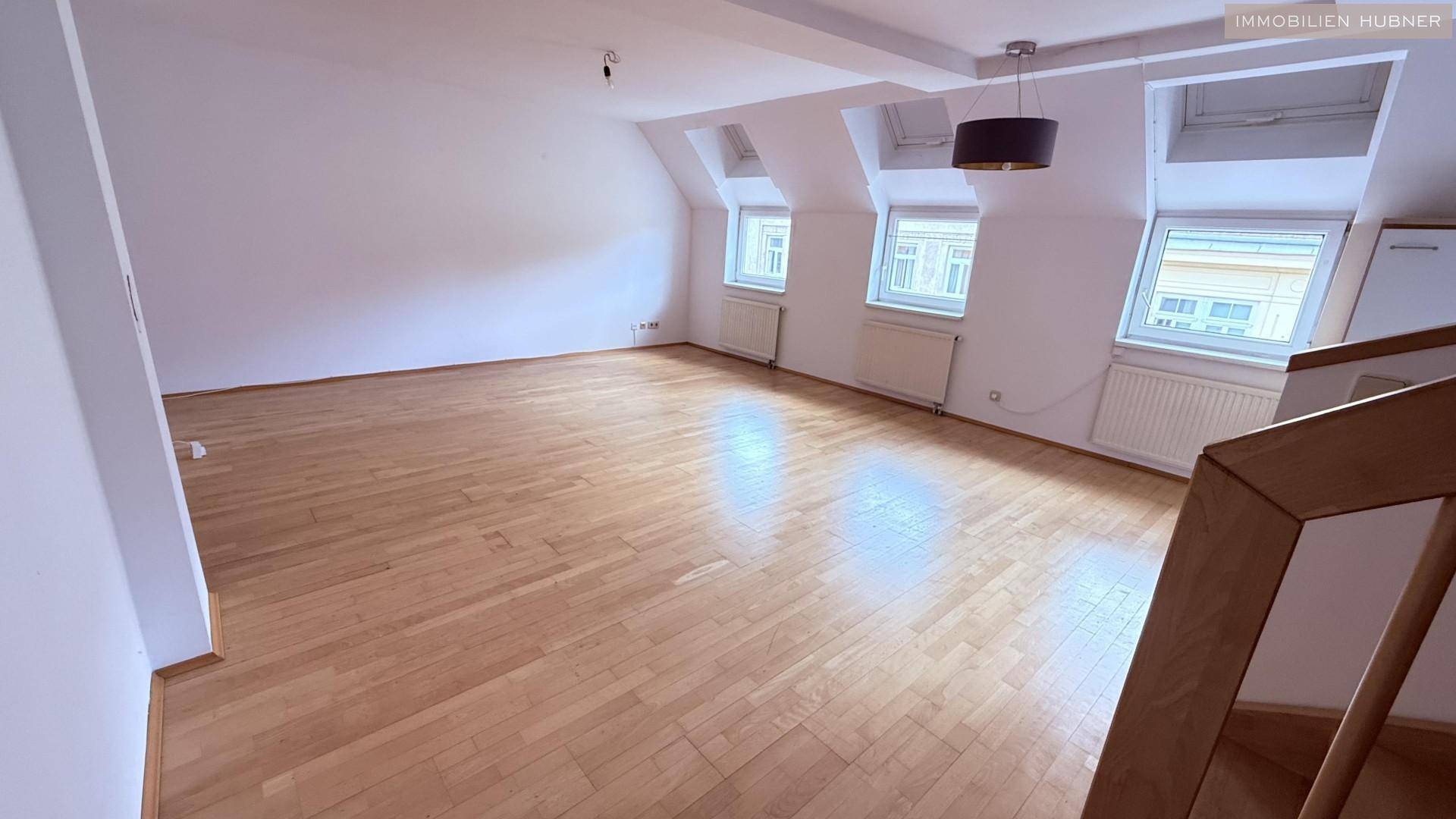 Heller Wohnraum mit Holzboden, Dachfenstern und Heizkörpern unter den Fenstern.