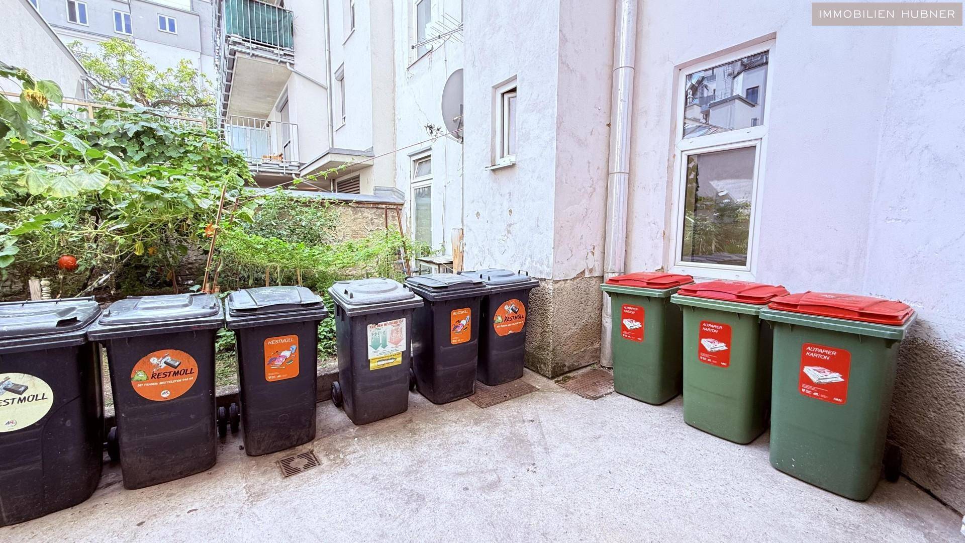 Hinterhofbereich mit Mülltonnen und einem kleinen Gartenabschnitt.