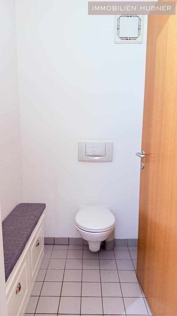 Separate Toilette mit Wand-WC, Fliesenboden und einer kleinen Sitzbank.