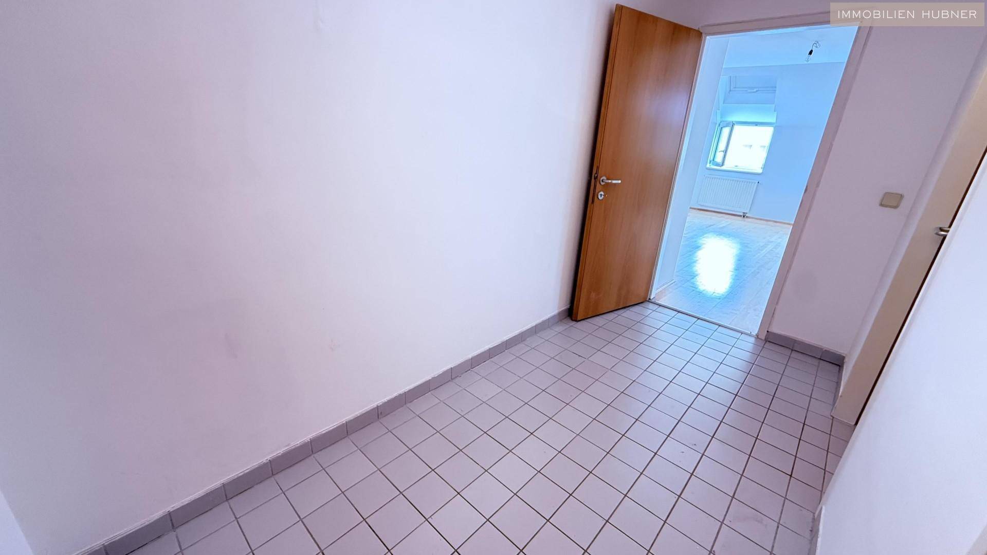 Flur mit Fliesenboden und einer offenen Tür, die den Blick in einen weiteren Raum freigibt.